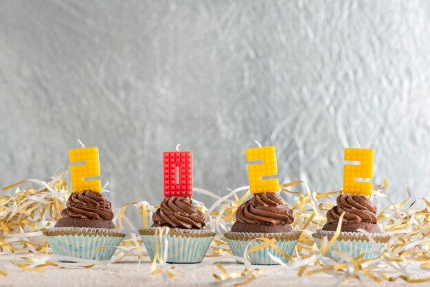 Cupcakes festivos de chocolate con crema de mantequilla decorados con 2022 números de velas. Fondo de lámina de plata. Copie el espacio.