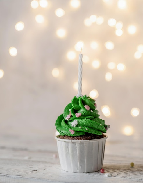 Cupcakes con forma de árbol de Navidad, rodeados de adornos festivos y luces de fondo