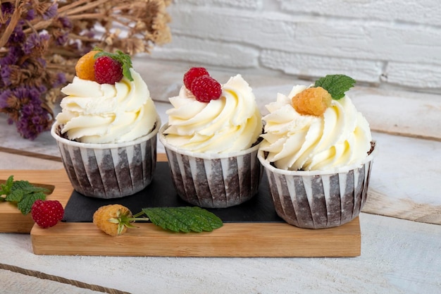 Cupcakes frescos com creme de queijo cremoso e frutas vermelhas em uma placa de madeira branca.