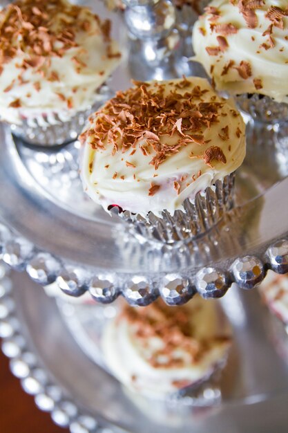 Cupcakes con glaseado blanco y cobertura de chocolate en bandeja de plata decorativa