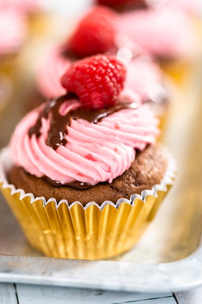 Cupcakes gourmet de chocolate y frambuesa rociados con ganache de chocolate y cubiertos con una frambuesa fresca.