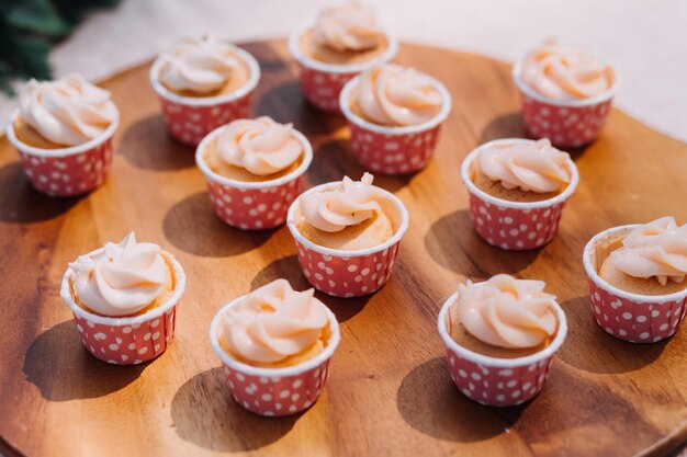 Cupcakes gourmet com cobertura de creme de manteiga branco e confeitos em fundo de madeira