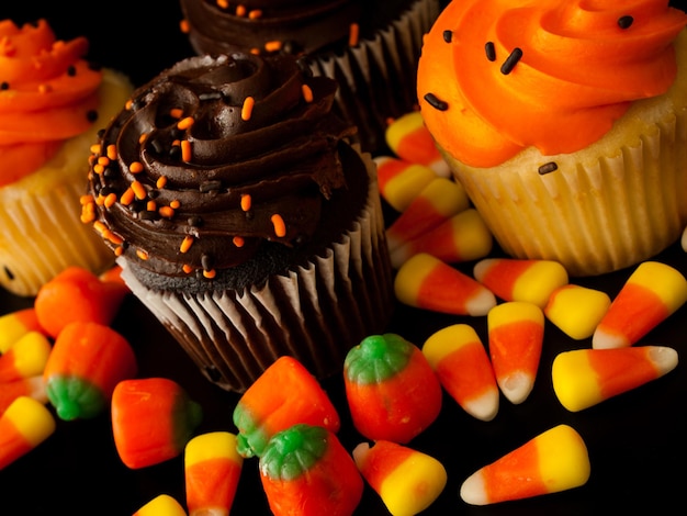 Cupcakes de Halloween naranja y negro con caramelos de maíz dulce sobre fondo negro.