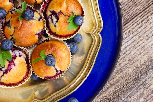 Cupcakes mit frischen Heidelbeerbeeren und Blättern auf silbernem und blauem Teller