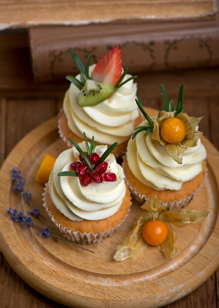 Cupcakes mit Sahne, dekoriert mit frischen Früchten auf einem Holztisch