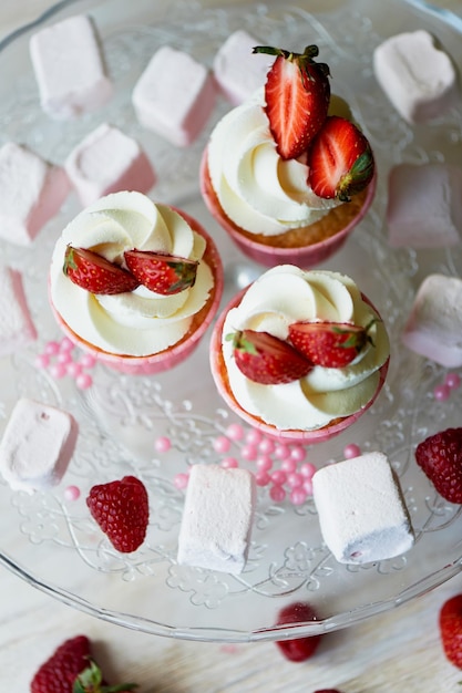 Cupcakes mit Schlagsahne und süßer Sahne, dekoriert mit Erdbeeren Auf einem Glasständer mit Marshmallows