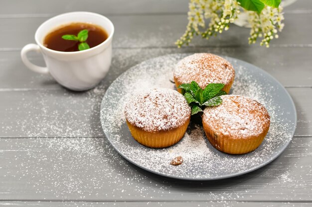 Cupcakes con pasas y una taza de té sobre un fondo de flores blancas