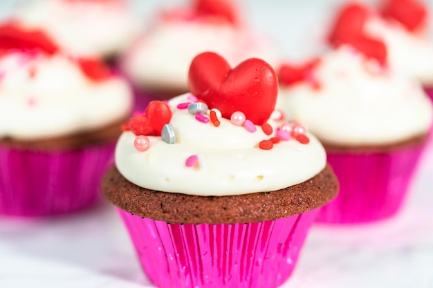 Cupcakes red velvet com cobertura de cream cheese e decorado com chocolates vermelhos em formato de coração e beijo