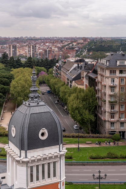 Cúpulas metálicas con agujas y pararrayos en el techo de una mansión con vistas a hermosos jardines, caminos, edificios antiguos y cielos nublados