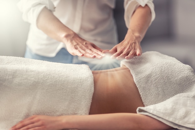 Foto cura esotérica pelas mãos de um terapeuta permanente, criando luz acima de uma jovem deitada de costas.