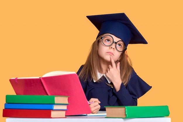 Curiosa colegiala en traje de graduación estudiando con libros de texto