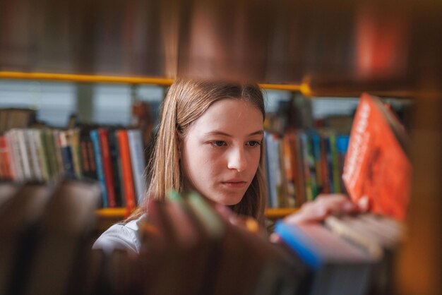 Curiosa estudante do ensino médio dentro da biblioteca escolhendo aleatoriamente livros das estantes Conceito de educação e conhecimento