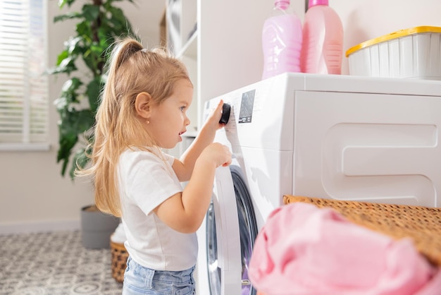 Curiosa linda niña de un año de edad, bebé pequeño jugando y encendiendo la lavadora