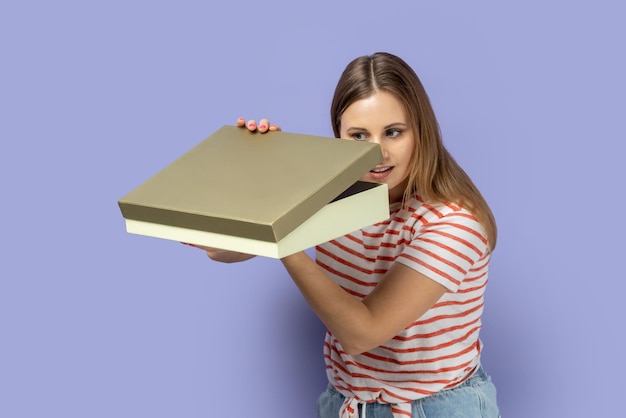 Curiosa mujer tranquila de pie sosteniendo la caja de regalo y mirando dentro interesante lo que hay dentro