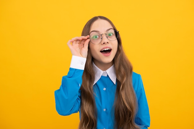 Curiosa niña en edad escolar mira a través de anteojos fondo amarillo curiosidad