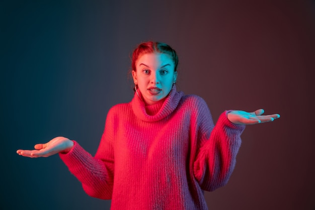 Curiosamente, fofo. Retrato da mulher caucasiana isolado no fundo do estúdio gradiente em luz de néon. Linda modelo feminino com cabelo ruivo. Conceito de emoções humanas, expressão facial, anúncio.