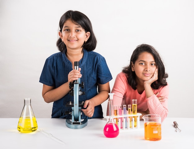 Curiosas niñas de la escuela india o científicos que estudian ciencias, experimentando con productos químicos o microscopio en el laboratorio, enfoque selectivo