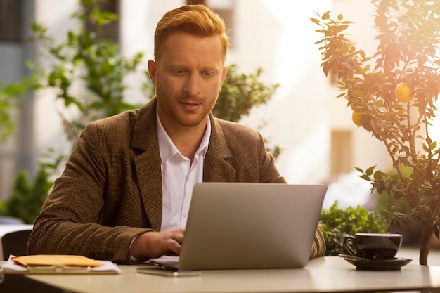 Curioso hombre de negocios concentrado mientras trabaja en la mesa con una computadora portátil