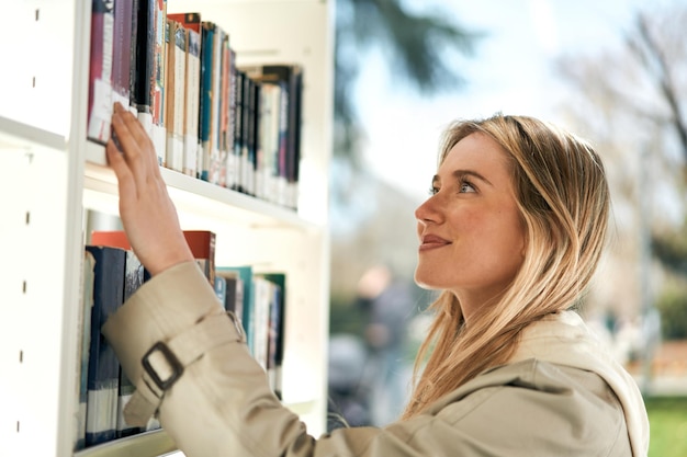 Curioso joven estudiante buscando un libro en una biblioteca en un soleado día de primavera