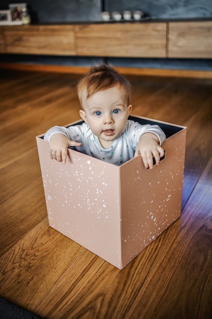 Curioso lindo niño rubio caucásico con hermosos ojos azules sentado en caja