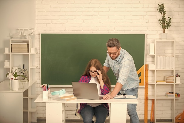 Curioso padre e hijo estudian en la escuela con una laptop en el fondo de la pizarra de regreso a la escuela