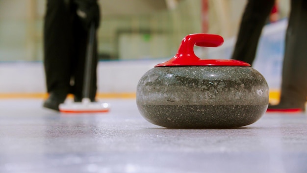 Curling entrenando una piedra de granito con mango rojo en el campo de hielo