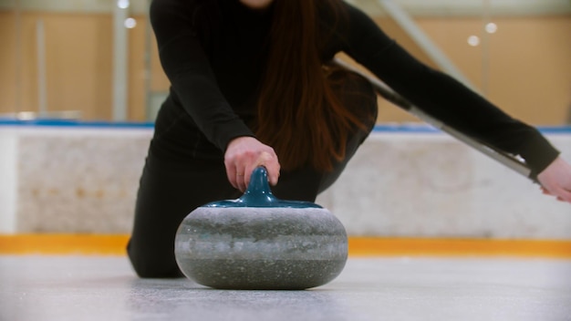 Curling segurando uma pedra de granito com alça azul no campo de gelo