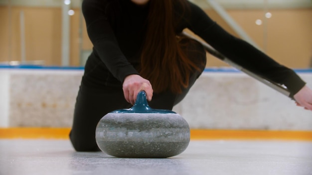 Curling sosteniendo una piedra de granito con mango azul en el campo de hielo