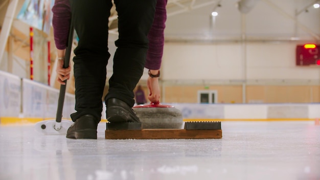 Curling-Training in der Halle eine Frau, die gerade dabei ist, den Stand auf dem Eisfeld abzustoßen