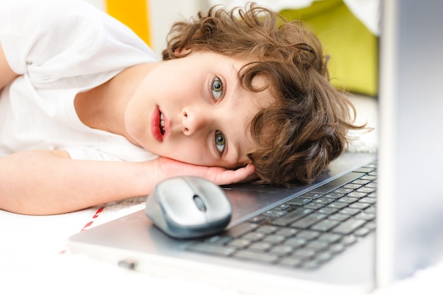 Foto curly boy ist am computer beschäftigt. müde kinderlügen bedecken sein gesicht mit den händen konzept der schwierigkeiten der heimschule, fernstudium