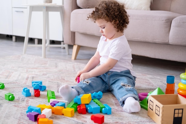 Curly Kind Mädchen spielen mit Pyramide und Konstrukteur zu Hause frühe Kinderentwicklung