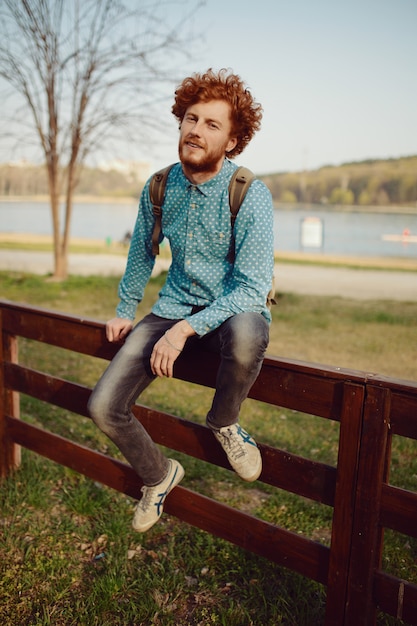 Curly Mann des Ingwers, der auf schöner Landschaft ruht