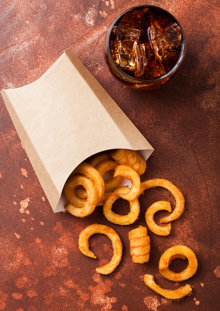 Curly Pommes Fast-Food-Snack im Papierbehälter mit Glas Cola auf rostiger Küche. Ungesundes Junk Food