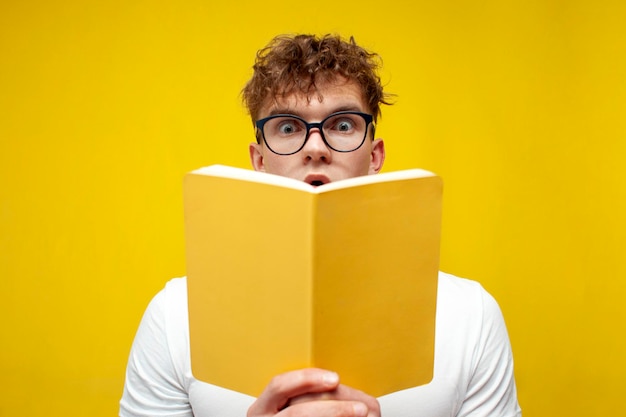 Curly schockierter Typ mit Brille liest ein Buch auf gelbem Hintergrund und zeigt Überraschung
