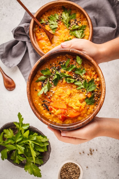 Curry indio amarillo de la sopa de lenteja del vegano con perejil y sésamo en un cuenco de madera en manos.