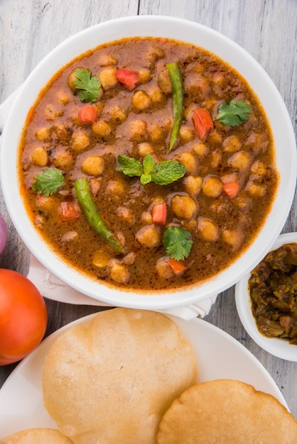 Curry picante de Chick Peas, prato indiano, também conhecido como Chola ou Chana Masala ou comumente Chole, servido com puri ou poori frito sobre fundo colorido ou de madeira. Foco seletivo