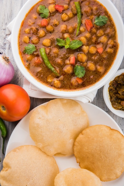 Curry picante de Chick Peas, prato indiano, também conhecido como Chola ou Chana Masala ou comumente Chole, servido com puri ou poori frito sobre fundo colorido ou de madeira. Foco seletivo