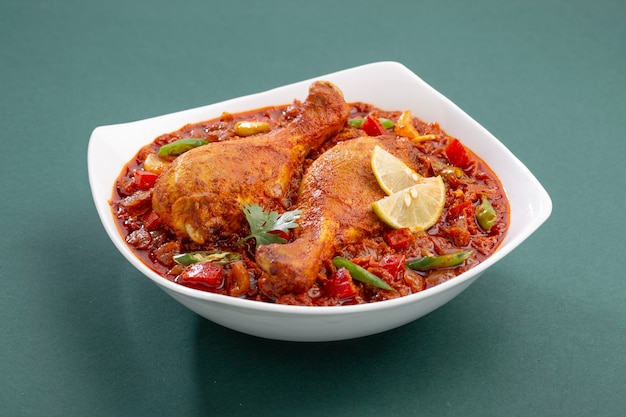 Curry de pollo indio o masala de pollo, salsa gruesa de pollo picante indio adornado con hojas de cilantro, rodajas de limón y dispuestas en una vajilla de cerámica blanca o en un tazón para servir sobre fondo verde, es