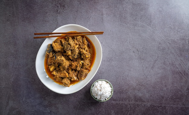 Curry de ternera casera en un tazón blanco con palillos y sal en la vista superior de baldosas de pizarra oscura