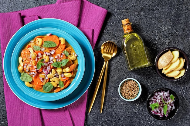 Curry de zanahoria clásico con anacardos y pasas en un recipiente azul sobre una mesa de hormigón, vista horizontal desde arriba, plano, espacio libre, cocina india