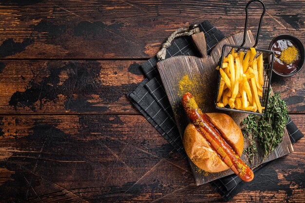 Currywurst Bratwurst im Brötchen mit Currysoße und Pommes frites. Hölzerner Hintergrund. Ansicht von oben. Platz kopieren.