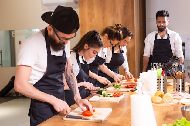 Curso de culinária chef masculino sênior em uniforme de cozinheiro ensina jovens alunos de aulas de culinária a se preparar