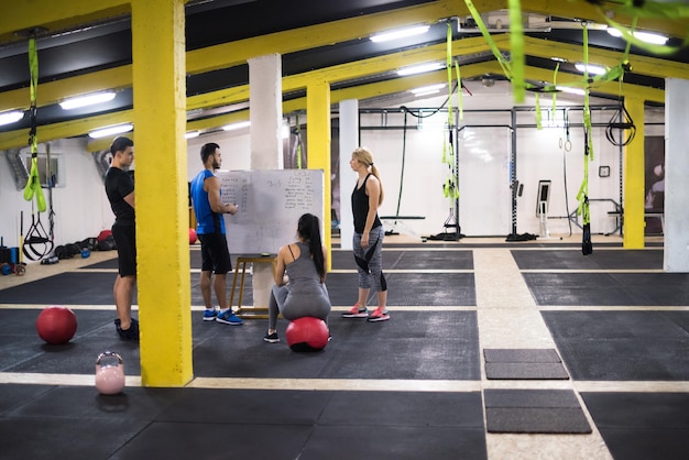 Curso de entrenamiento. grupo de atletas jóvenes que reciben instrucciones del entrenador antes de hacer ejercicio en el gimnasio cross fitness