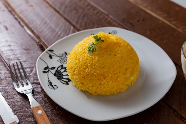 Cuscuz con queso, comida típica del noreste en un plato blanco y mesa de madera