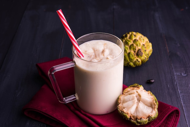 Custard Apple ou Sitafal Milk Shake servido em um copo com frutas inteiras sobre um fundo temperamental. Foco seletivo