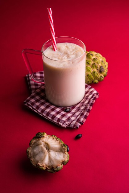 Custard Apple ou Sitafal Milk Shake servido em um copo com frutas inteiras sobre um fundo temperamental. Foco seletivo