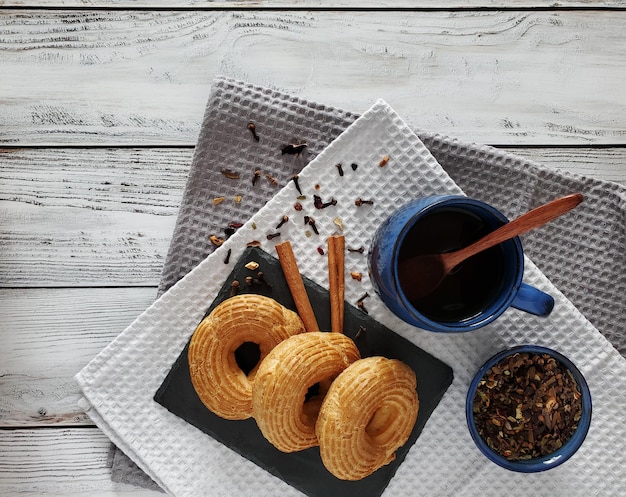 Custard-Ringe mit Hüttenkäse und Tasse Tee mit Zimt auf hellem Holzhintergrund