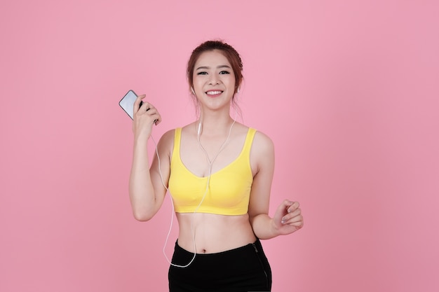 Cute asiatischen Mädchen hören Musik auf Smartphone über Kopfhörer, gesunde Fitness Lifestyle-Konzept mit rosa Hintergrund isoliert