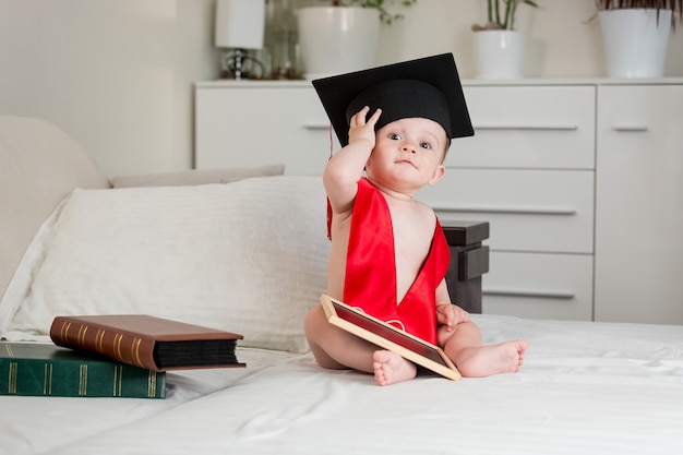 Cute Baby Boy en mortarboard académico sentado en la cama