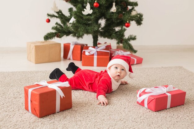 Cute Baby Girl vistiendo traje de Santa Claus arrastrándose por el suelo junto al árbol de Navidad